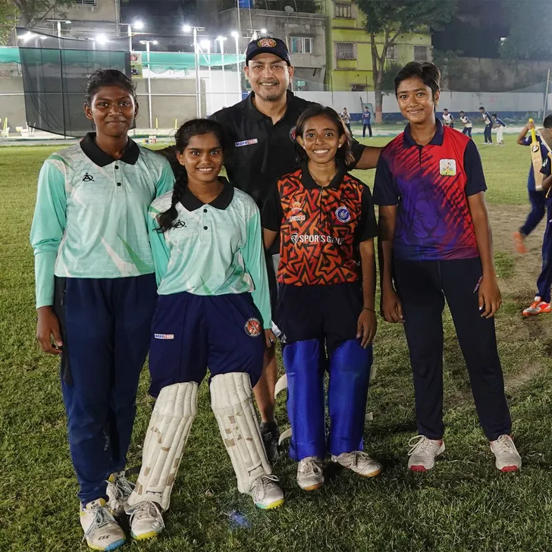 Four women cricketers with their coach under the floodlights at Harvard House Sports